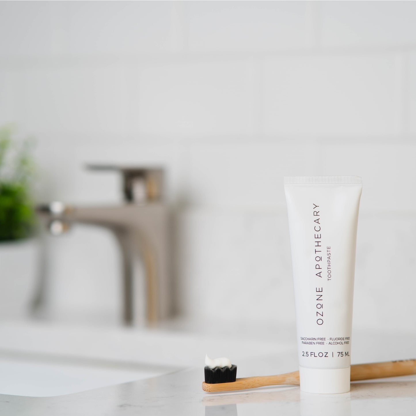 Ozone Apothecary toothpaste tube and bamboo toothbrush on a bathroom counter.