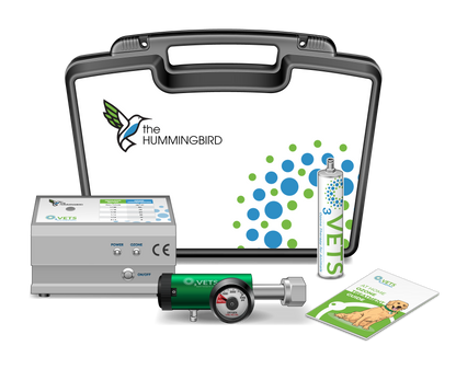 A collection of items including a Hummingbird Ozone Generator, a pediatric oxygen regulator, tubing, a hydrophobic valve, a 3-way stopcock, a carry case, and training materials. The items are displayed with the brand 'The Hummingbird' visible on the case and the generator.